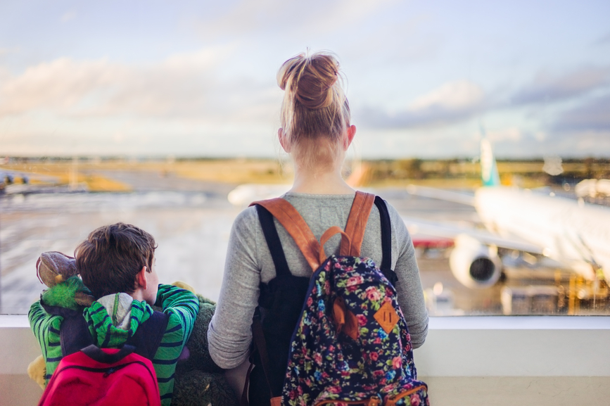 Two children look out an airport window at the plane they are waiting to board