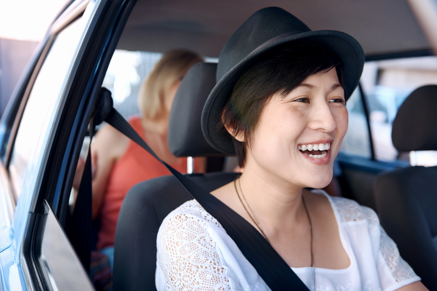 A laughing pretty chinese woman with a hat on driving somewhere with her friends in the backseat