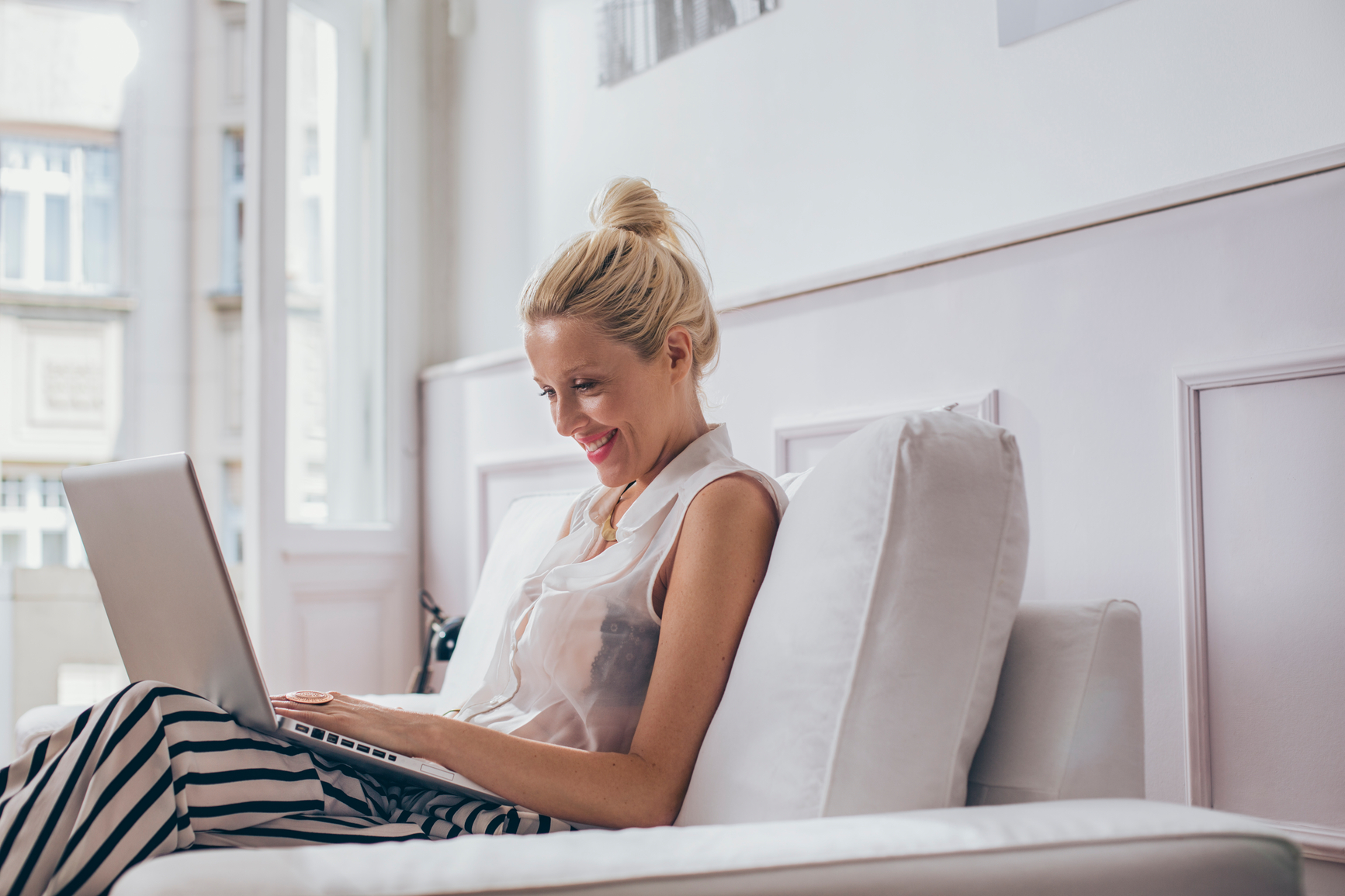 Smiling Caucasian woman sitting on her sofa and using her laptop.