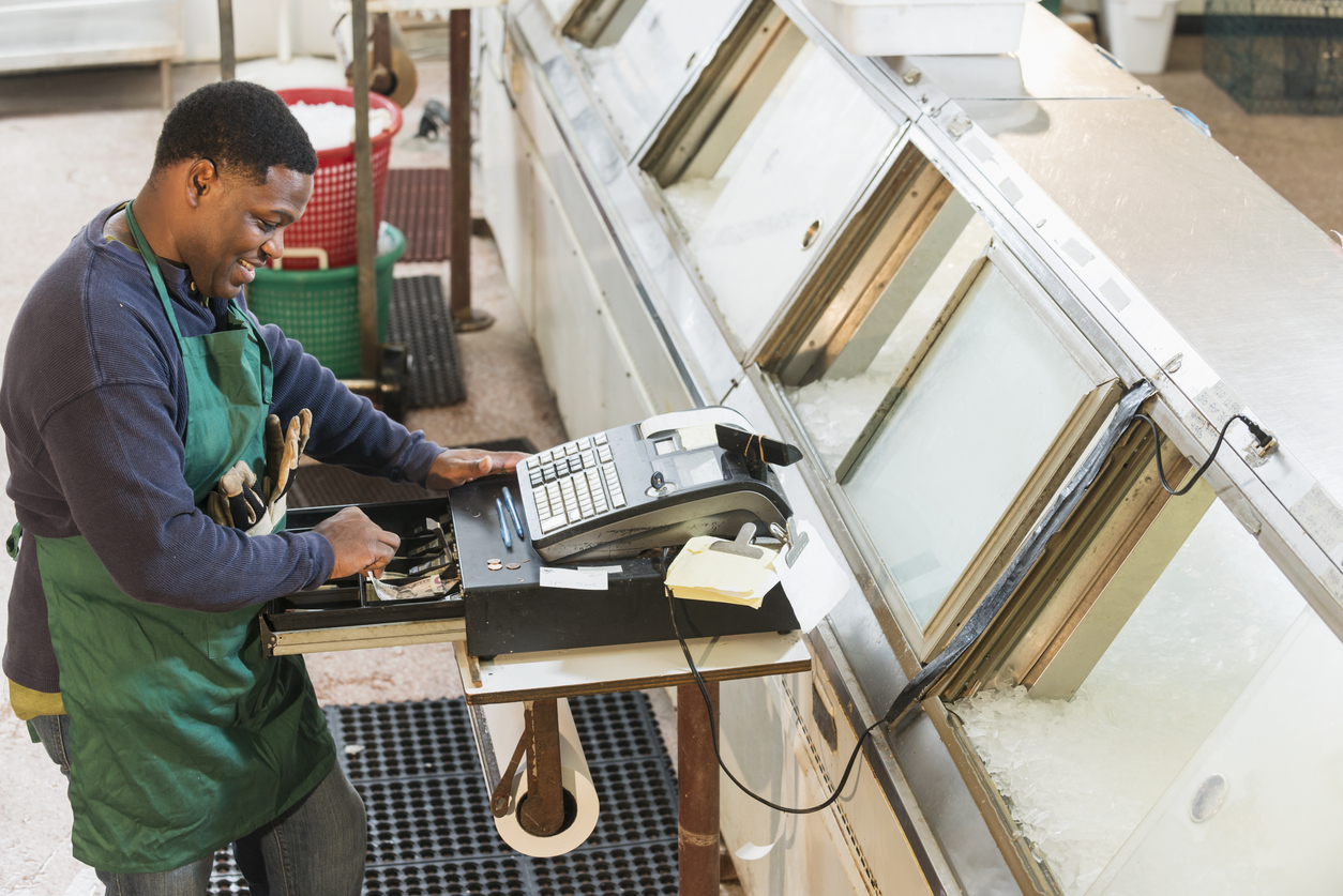 An African American man working in a fish market. He is at the cash register, taking money out to make change.